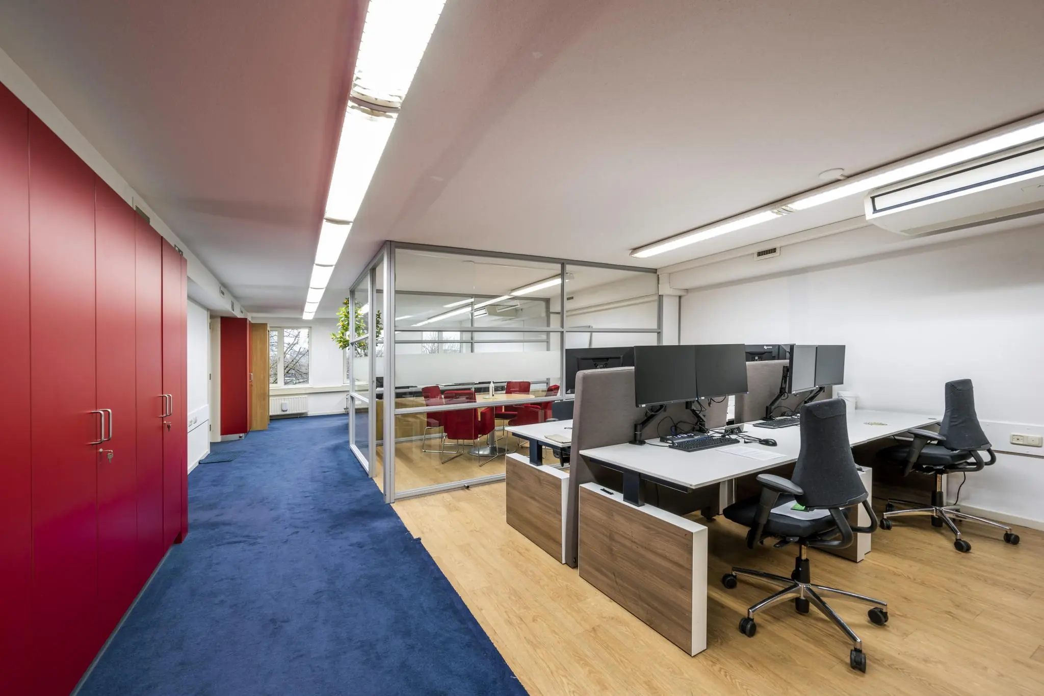 Moderne kantoorruimte aan de Prins Hendrikkade met werkplekken, glazen vergaderruimte en felrode kasten.